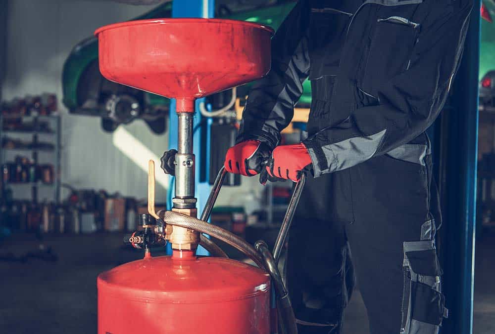 Mechanic using specialized tool to perform an oil and filter change on a car engine.