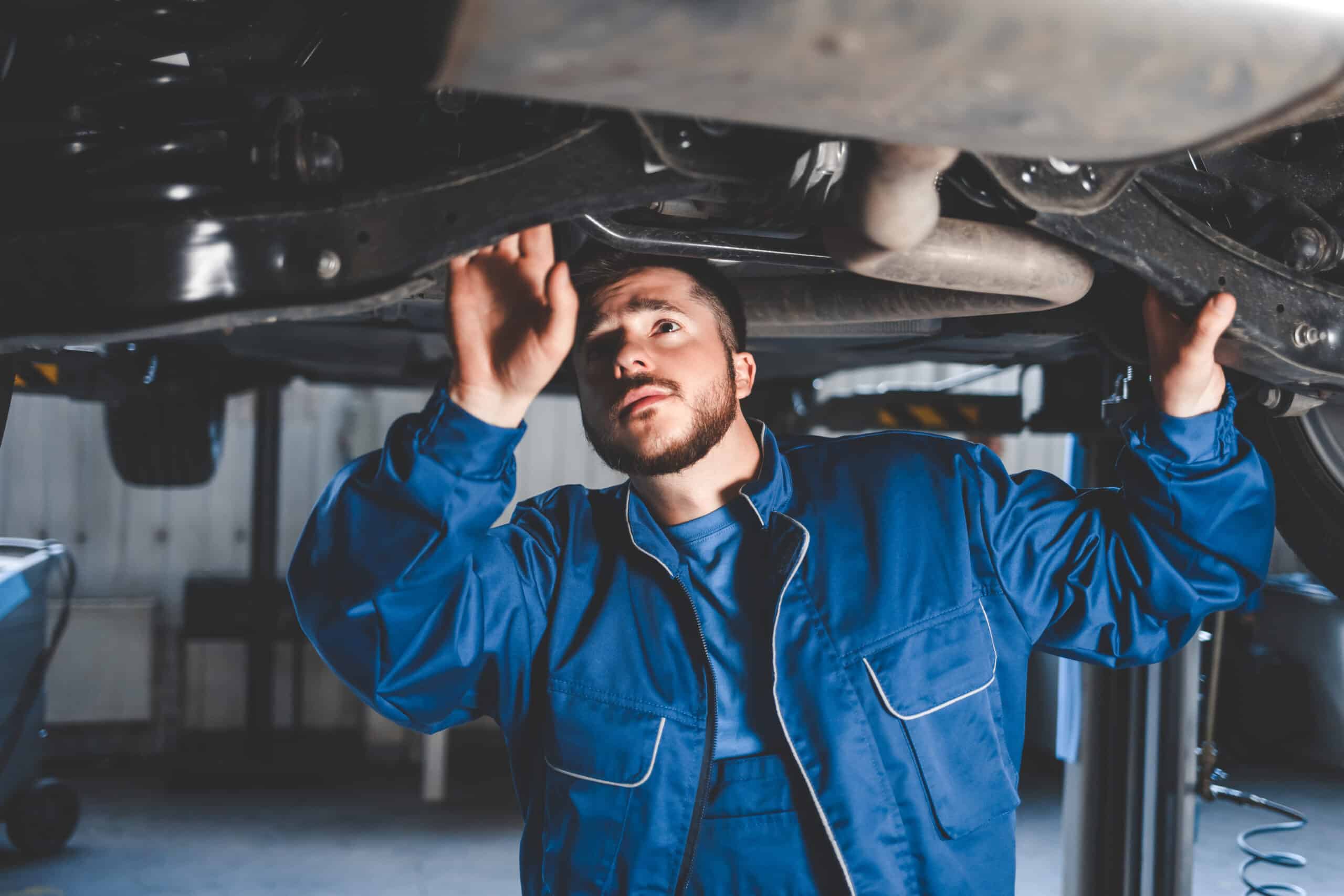 An auto mechanic examines the steering and suspension of a car during a thorough inspection.