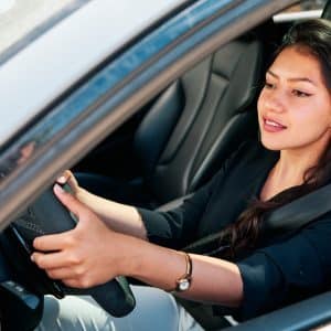 Latin woman driving car, offering driving tips for beginners.